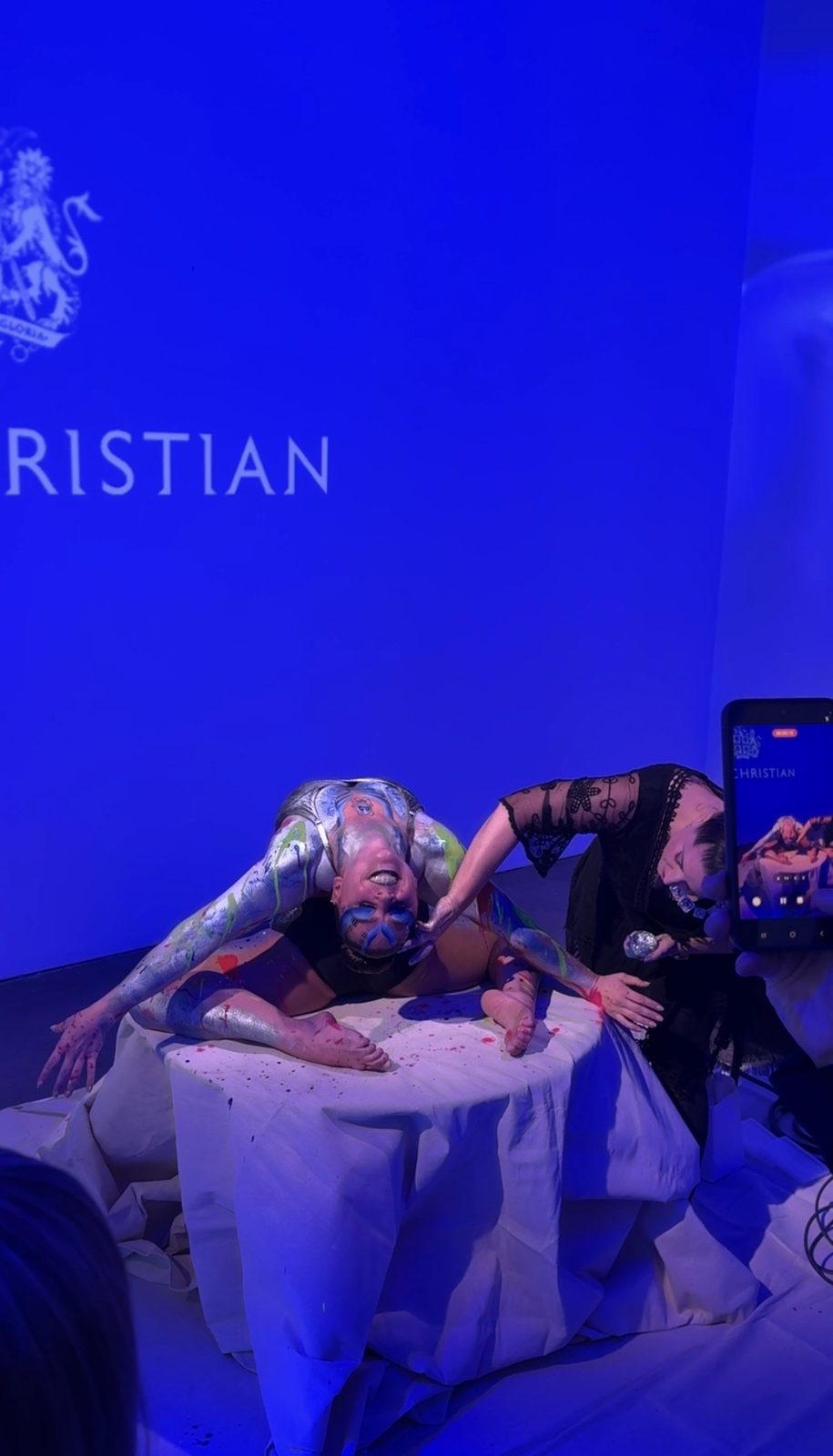 Body-painted contortionist in a deep backbend as the artist adds finishing touches