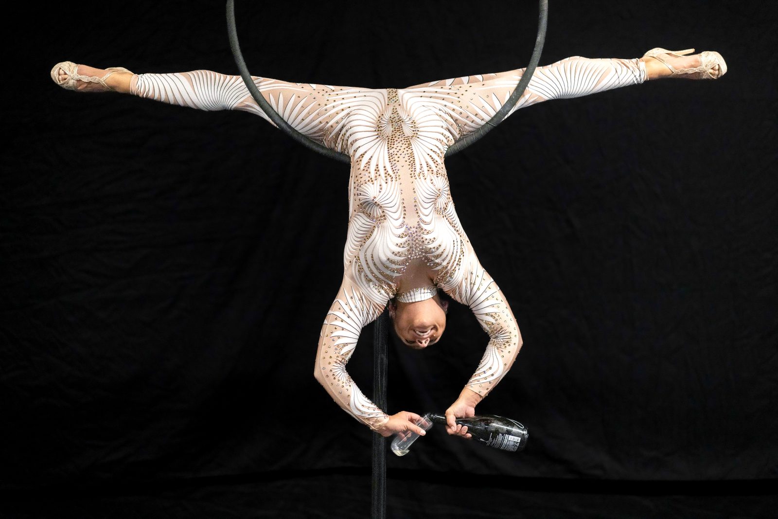 Inverted split on the aerial hoop, pouring champagne into a glass