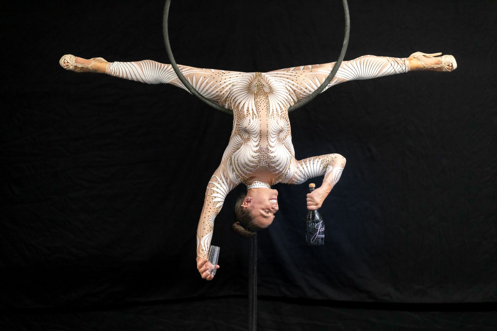 Upside-down on the aerial hoop with a champagne bottle and glass
