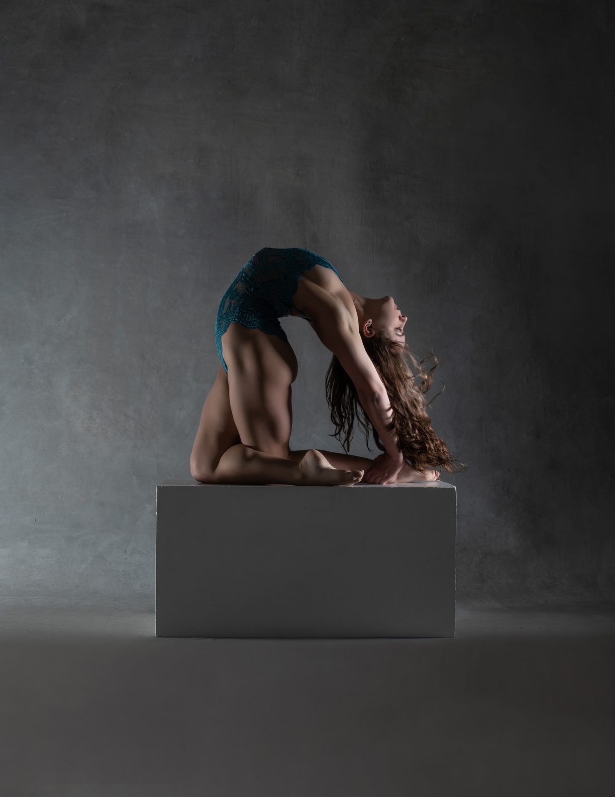 Contortion backbend on a pedestal in a grey studio
