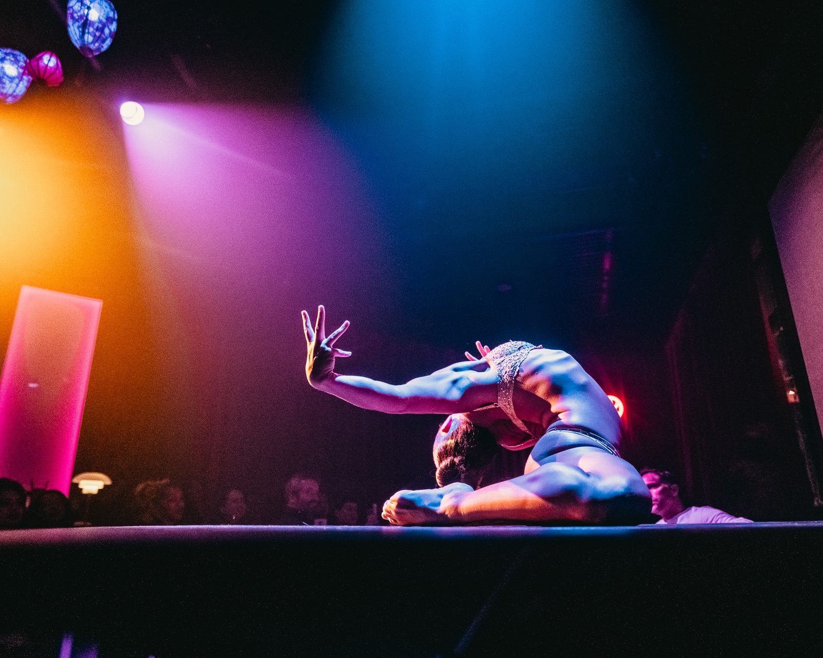 Allison Schieler in a deep contortion backbend on stage under pink and blue light