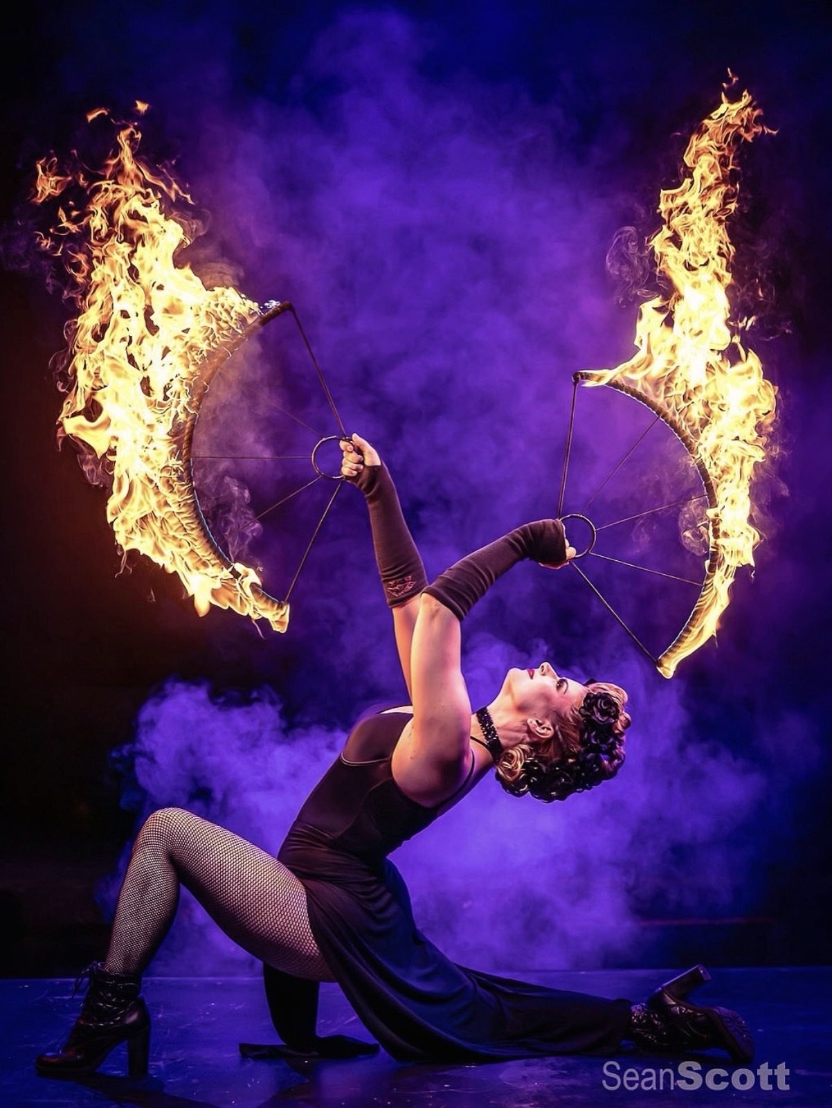 Fire performer sweeping twin flames through purple smoke