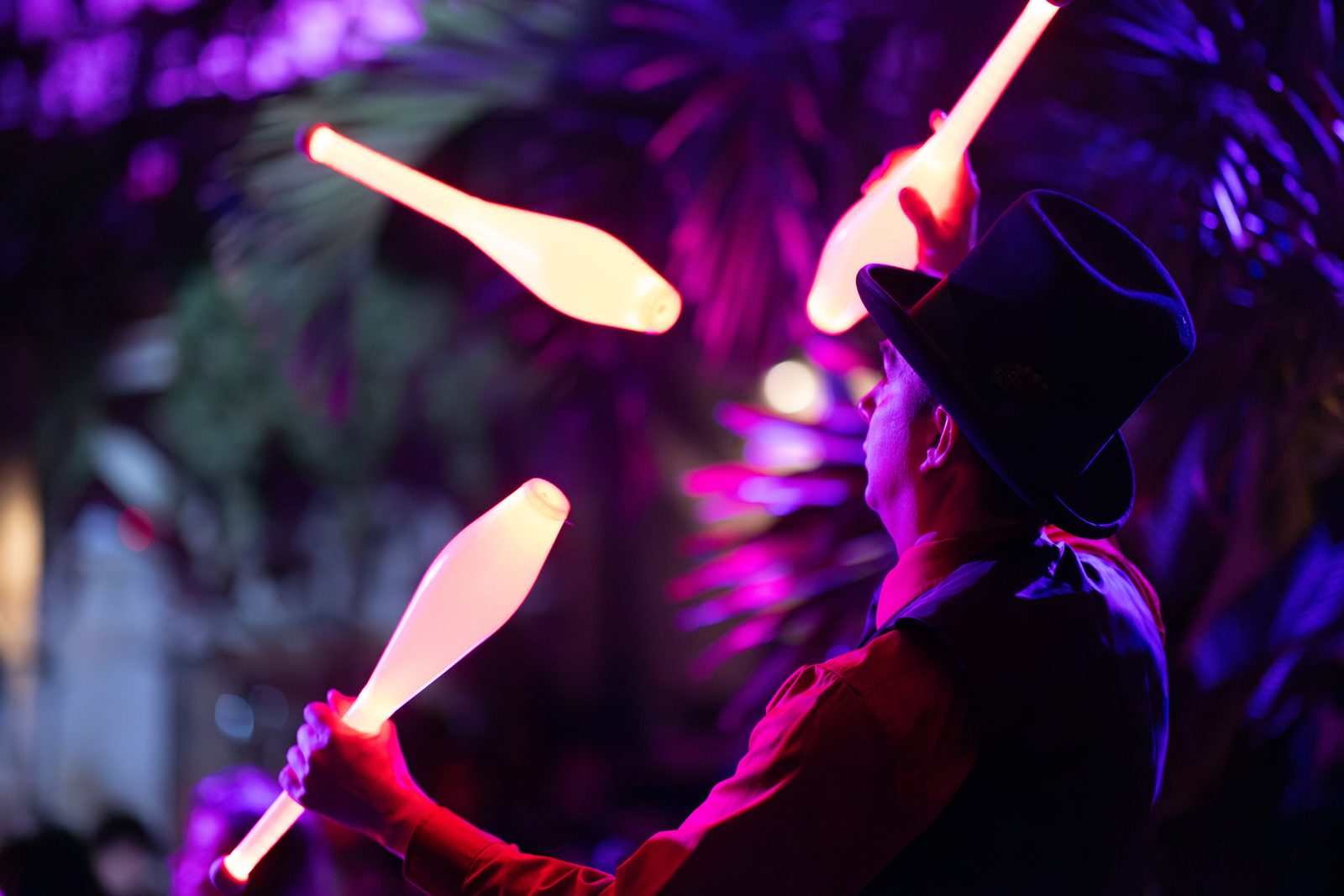 Juggler mid-pattern with glowing clubs under palm fronds