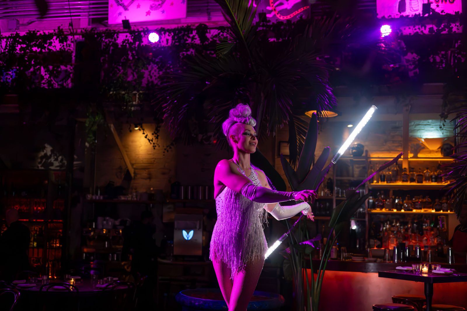 LED poi performers spinning light trails at a purple-lit venue
