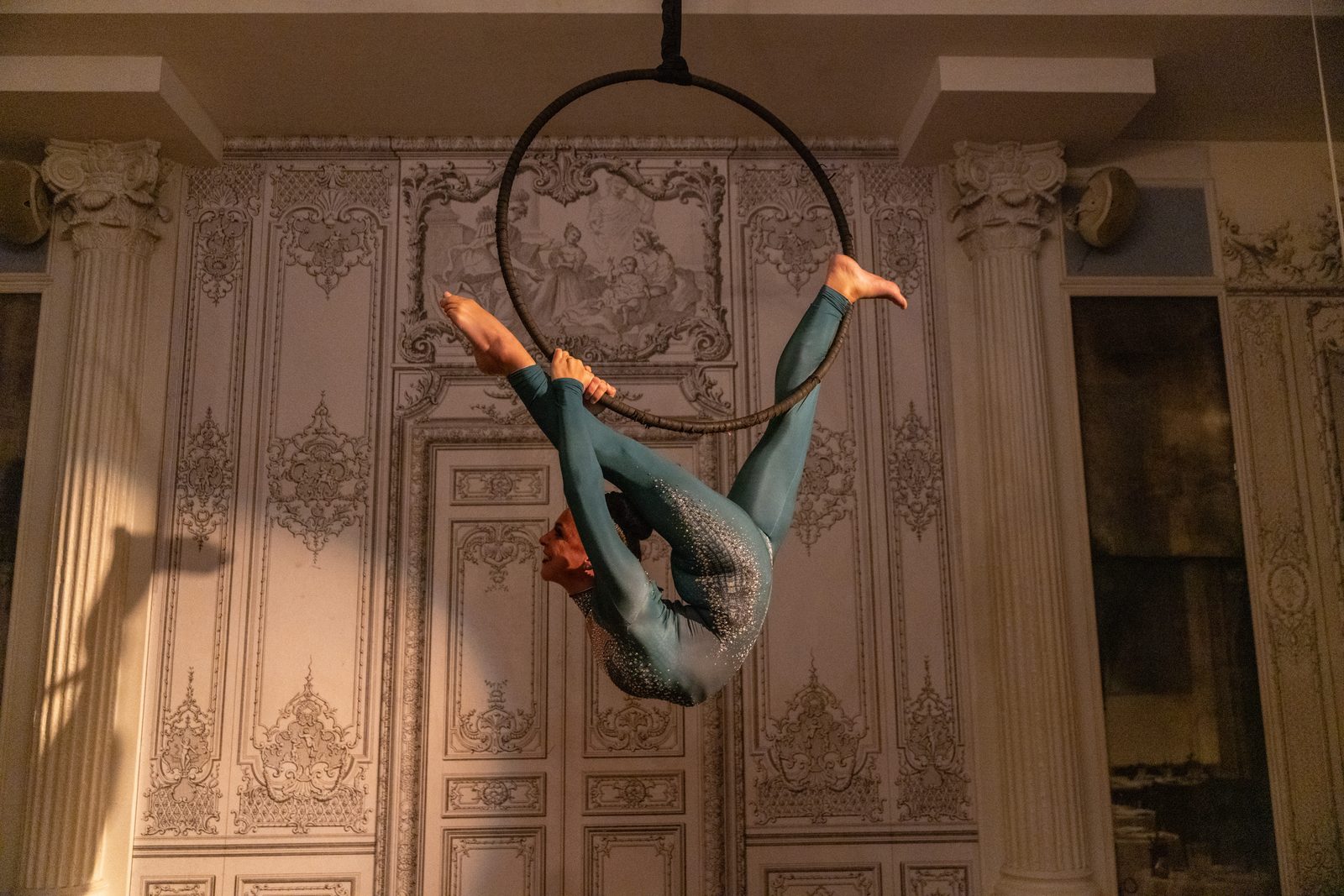 Straddle pose on an aerial hoop in a gilded room
