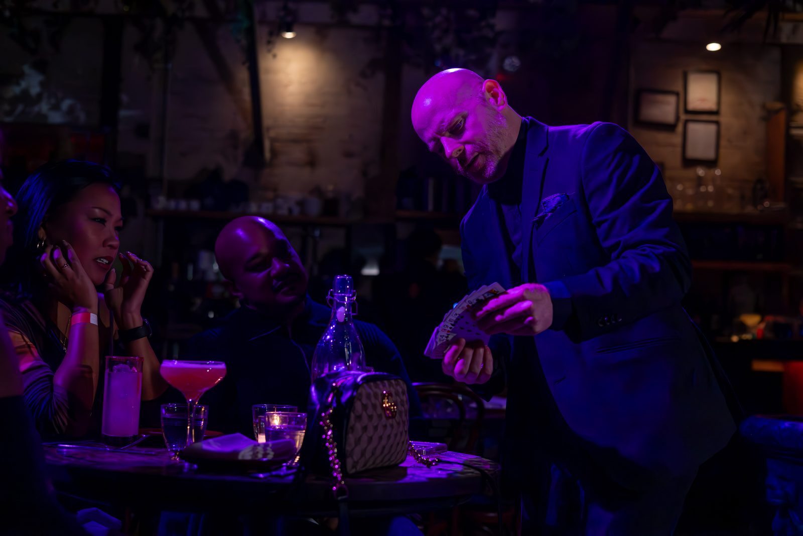 Magician performing card magic for guests at a dim lounge